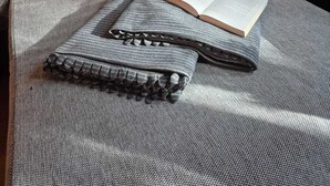 Une pièce chaleureuse avec un plafond en bois, un lit recouvert d’une couverture grise, un oreiller orné d  ’un motif de cerf et une fenêtre donnant sur les arbres.