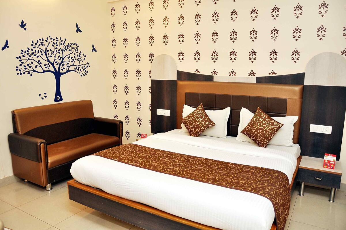 A hotel room with a large bed, a wooden headboard, and a brown leather sofa.