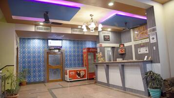 A hotel lobby with a reception desk, a Coca-Cola refrigerator, a television, and patterned walls.