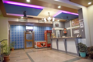 A hotel lobby with a reception desk, a Coca-Cola refrigerator, a television, and patterned walls.
