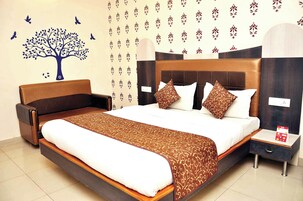 Habitación de hotel con una cama grande, una mesita de noche, una silla y una pared con un adhesivo de árbol y papel tapiz estampado.