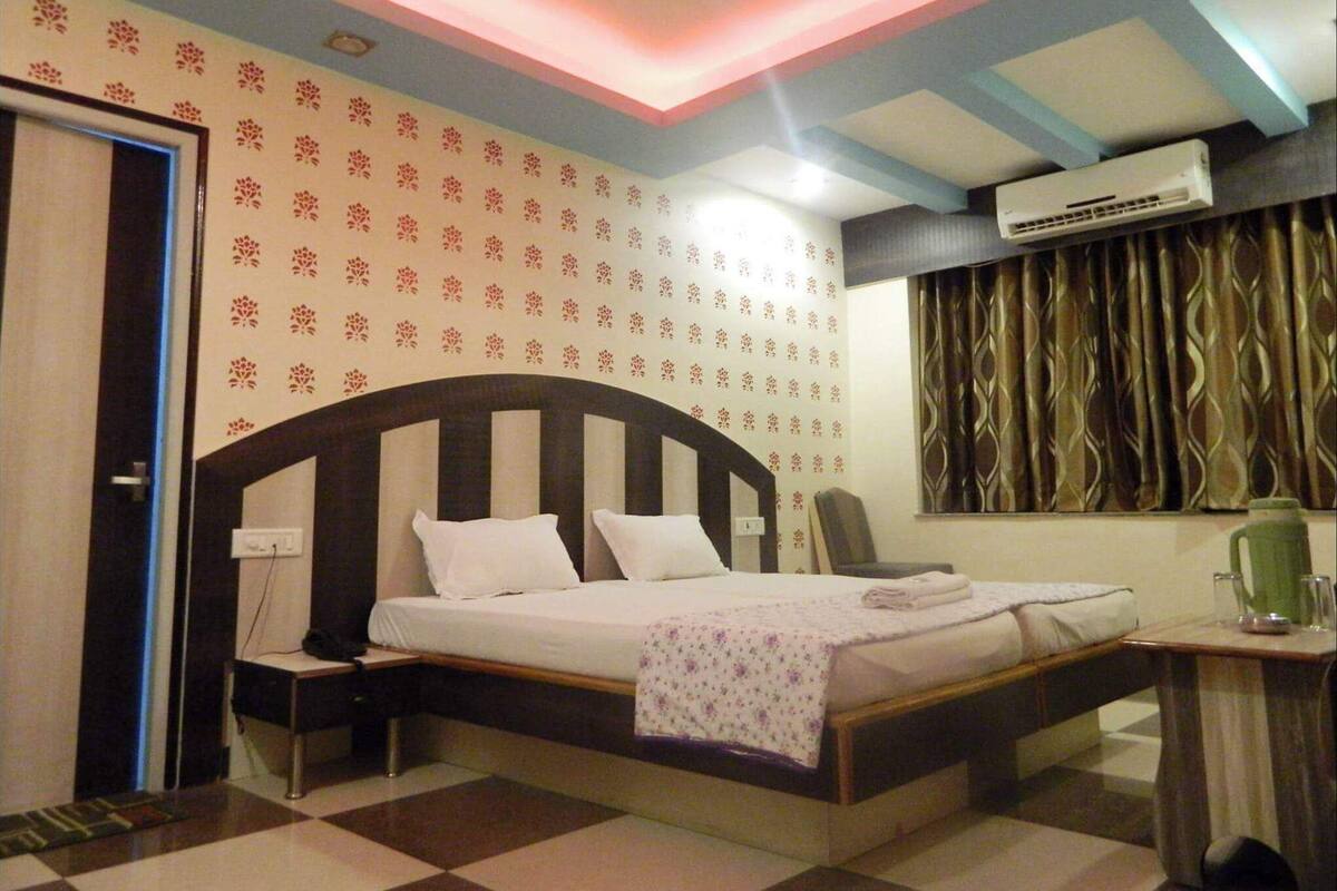 A bedroom with a bed, nightstand, chair, and an air conditioning unit.