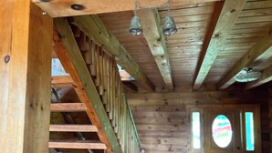 Un escalier en bois avec une rampe en métal, des murs en bois et une porte dotée d’une fenêtre ronde.