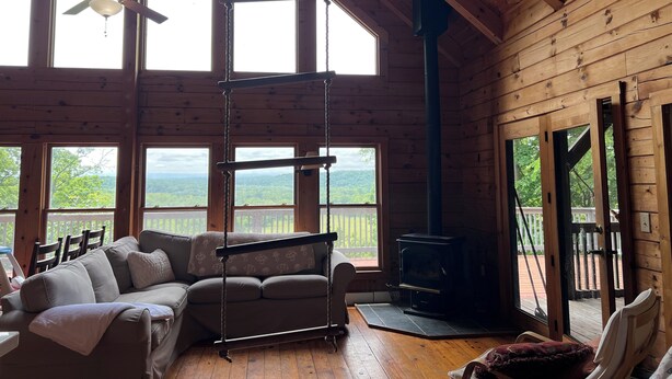 Une cabane avec un grand intérieur en bois, un canapé, une balançoire, une cheminée et une vue sur l’extérieur.