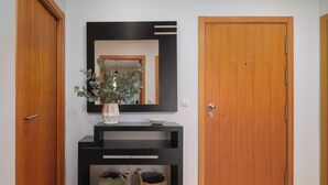 A hallway with a wooden door, a black console table with a vase and two baskets, and a mirror on the wall. - HALT Apartment (Ponta Delgada)