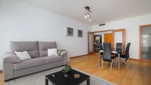 A living room with a grey sofa, a black coffee table, and a dining area with a glass table and black chairs. - HALT Apartment (Ponta Delgada)
