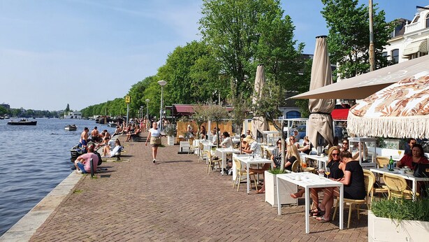 Un espace de restauration au bord de la rivière, avec des tables, des chaises et des parasols à l'extérieur.