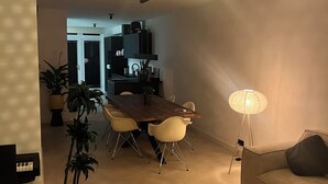 Un salon moderne avec un coin repas, comprenant une table en bois, des chaises beiges, un canapé et un lampadaire.