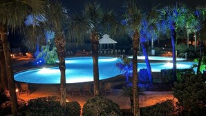 A nighttime view of a swimming pool surrounded by palm trees and a gazebo. - Crescent 109 (Miramar Beach)