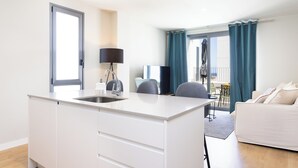 A modern kitchen with a sink, a dining area with chairs, a sofa, and a balcony with curtains. - Modern apartment near the sea in Tenerife. (Abades)