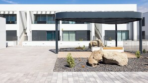 A modern building with a covered outdoor area, large rocks, and small plants. - Modern apartment near the sea in Tenerife. (Abades)