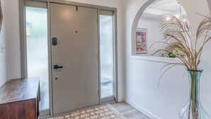 A hallway with a wooden door, a glass vase with dried plants, and a hanging light fixture. - Upscale Fishers Getaway/Hot Tub/Peaceful/Quiet! (Fishers)