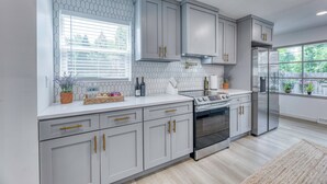 A modern kitchen with grey cabinets, a stainless steel stove, and a refrigerator. - Upscale Fishers Getaway/Hot Tub/Peaceful/Quiet! (Fishers)