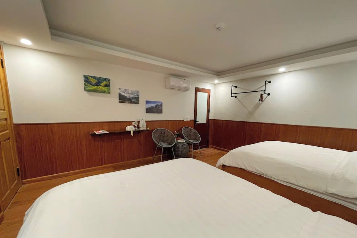 A hotel room with two beds, a wooden panel wall, a small desk with a telephone, and a chair.