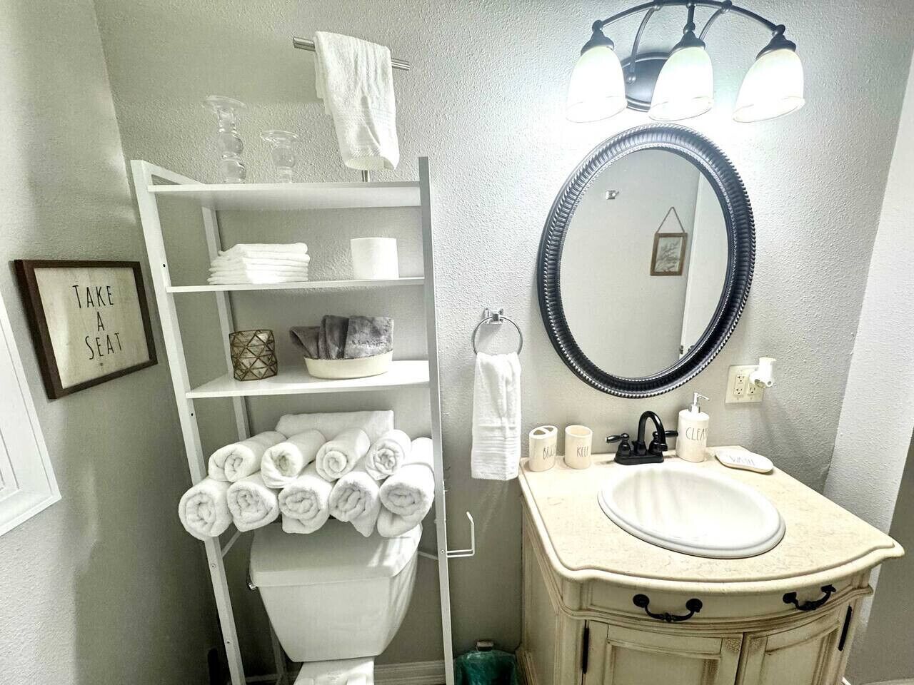A bathroom with a white vanity, a round mirror, and a towel rack with neatly folded towels.