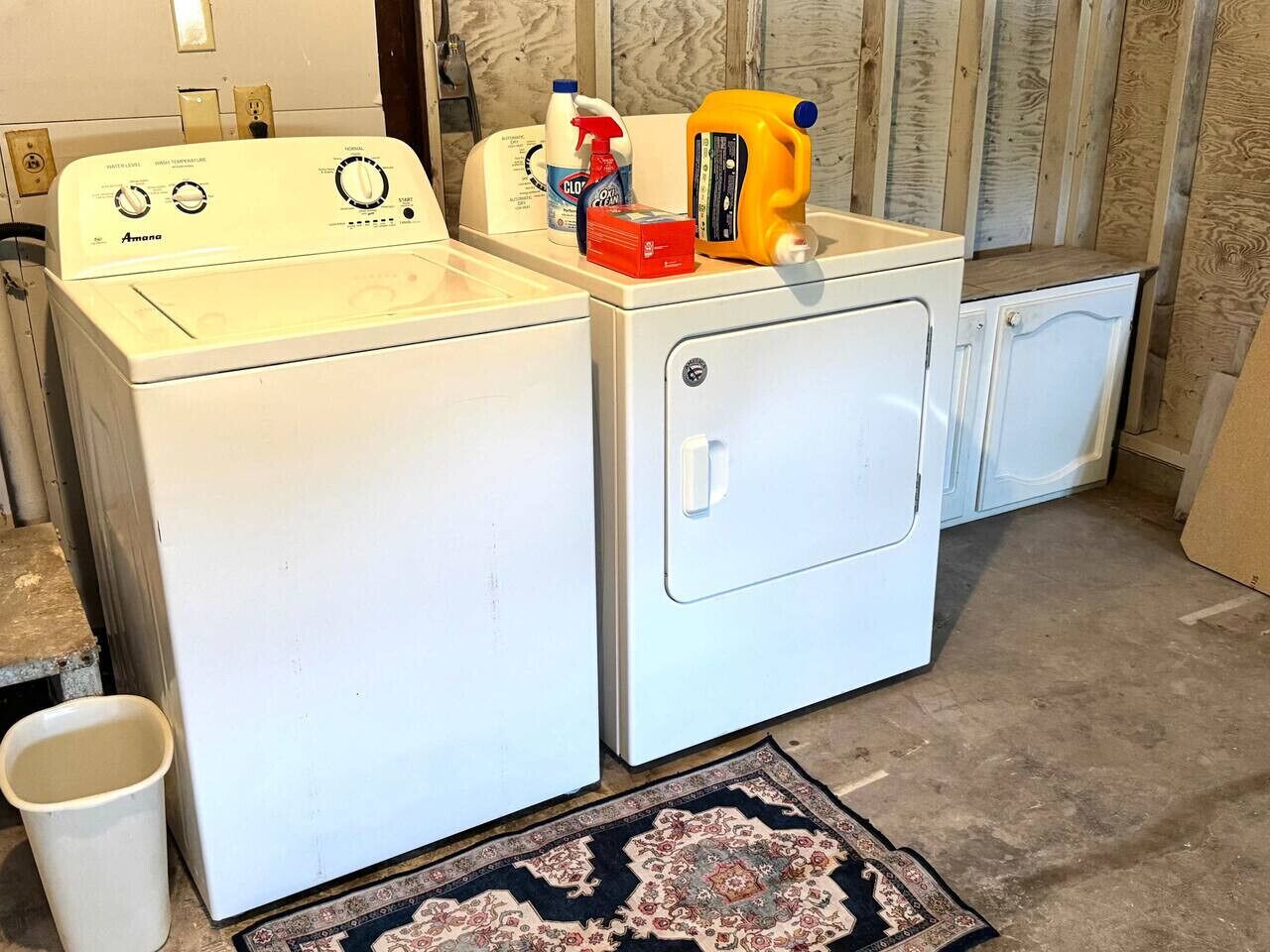Une buanderie équipée d’un lave-linge et d’un sèche-linge à chargement frontal, d’un petit tapis et de produits de nettoyage posés sur le sèche-linge.