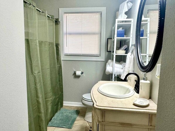 Une salle de bain avec un rideau de douche, des toilettes, un lavabo avec un miroir et un porte-serviettes.
