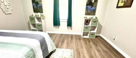 A bedroom with a bed, a dresser, a nightstand, a window with curtains, and a painting on the wall.