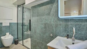 A modern bathroom with a glass shower enclosure, a white sink, and a marble-tiled wall. - Amazing studio Le Marais (Paris)