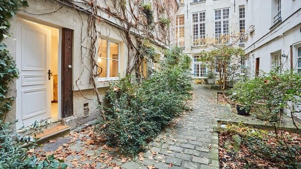 A narrow cobblestone alley with a building on one side and a tree-lined path on the other. - Amazing studio Le Marais (Paris)