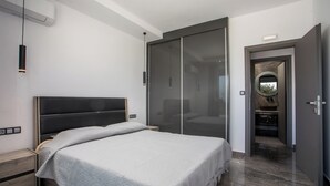 Ein modernes Schlafzimmer mit einem großen Bett, einem Schiebetürenschrank und einem durch eine offene Tür erreichbaren Badezimmer.