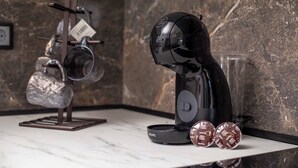Eine Küchenarbeitsplatte mit einer Kaffeemaschine, einem hängenden Wasserkocher und zwei Kaffeekapseln.