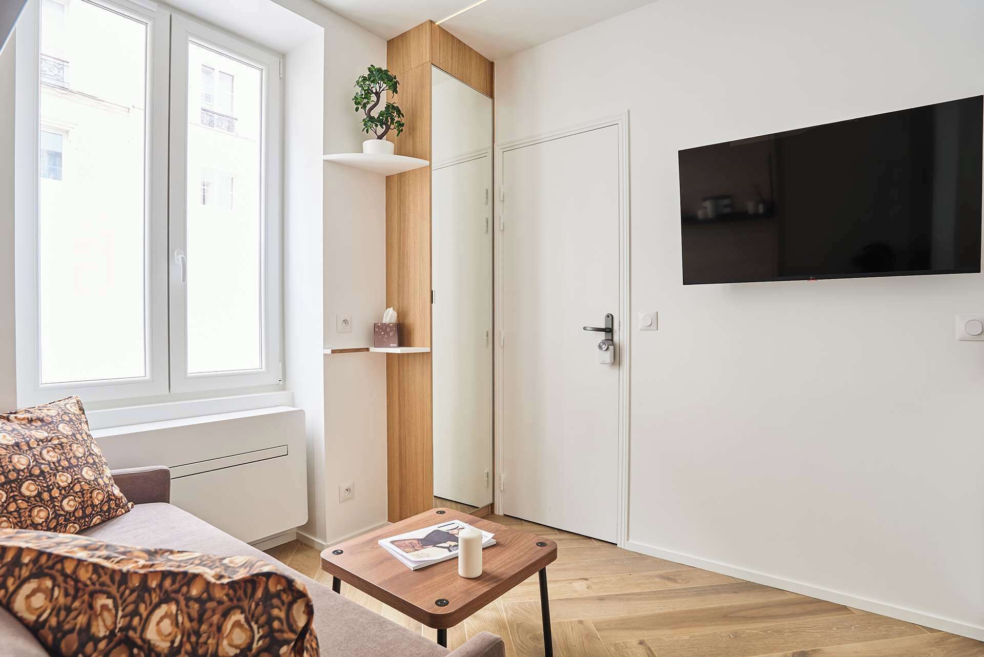 Un salon moderne comprenant un canapé, une table basse, un téléviseur fixé au mur et une porte avec un panneau en bois.