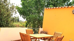 A patio with a wooden table and chairs, surrounded by a yellow wall and trees. - [Caracol 4] Apartment in the middle of the countryside with terrace (Orosei)