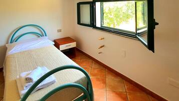Un dormitorio pequeño y ordenado con una cama, una mesita de noche, una ventana con vistas a zonas verdes y un suelo de baldosas.