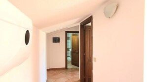 A narrow hallway with a tiled floor, a wooden door, and a wall-mounted light fixture. - [Caracol 4] Apartment in the middle of the countryside with terrace (Orosei)