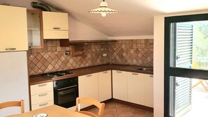 A compact kitchen with a dining table, cabinets, a stove, and a window with blinds. - [Caracol 4] Apartment in the middle of the countryside with terrace (Orosei)
