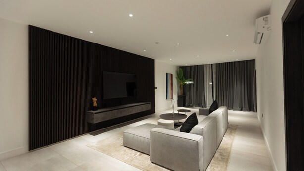 A modern living room with a flat-screen TV, grey sofas, a coffee table, and a dark accent wall.