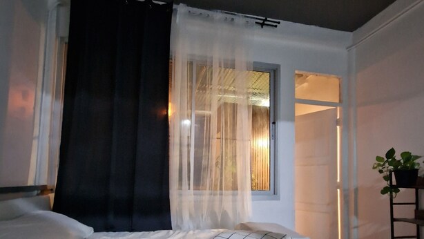 A bedroom with a bed, sheer curtains, a window, and a potted plant. - 4-bedroom hotel in peaceful Krung Thep Maha Nakhon with AC, WiFi (Krung Thep Maha Nakhon)