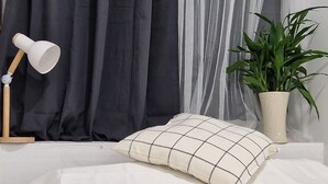 A neatly made bed with a checkered pillow, a bedside lamp, and a potted plant. - 4-bedroom hotel in peaceful Krung Thep Maha Nakhon with AC, WiFi (Krung Thep Maha Nakhon)