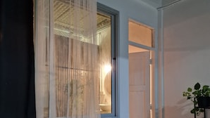 A bedroom with a bed, a window with sheer curtains, a bedside plant, and a door leading to another room. - 4-bedroom hotel in peaceful Krung Thep Maha Nakhon with AC, WiFi (Krung Thep Maha Nakhon)