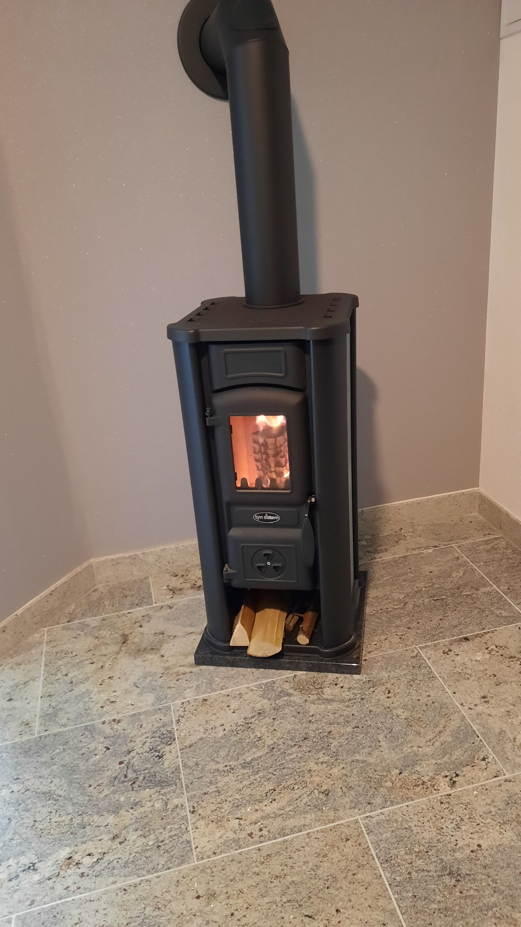 A wood-burning stove with a chimney, placed on a tiled floor.