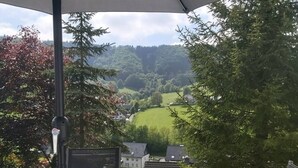 Une table ronde en verre avec un cadre en métal, une chaise noire et un grand parasol qui offre de l’ombre.