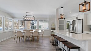 Una cocina moderna con una isla grande, muebles blancos y una zona de comedor con mesa y sillas.