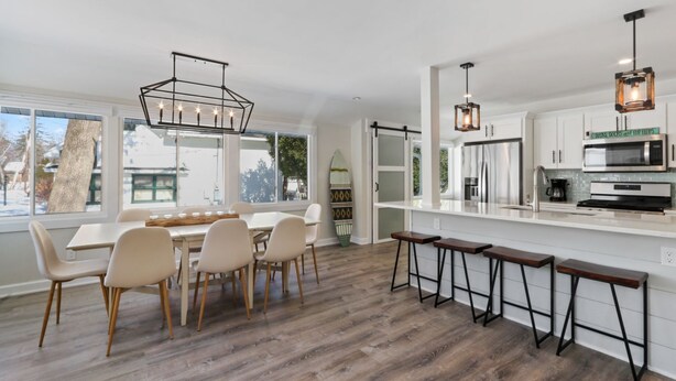 Una cocina moderna con armarios blancos, una isla central, taburetes de bar e iluminación colgante.