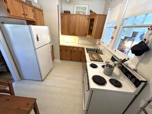 A kitchen with wooden cabinets, a white refrigerator, a stove, and a window with a view. - Cottage Near Beach and Boards, Cottage Near Beach and Boards (Ocean City)