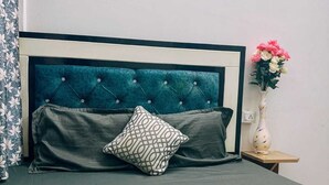 A neatly made bed with a teal headboard, a patterned pillow, and a floral arrangement on a bedside table.