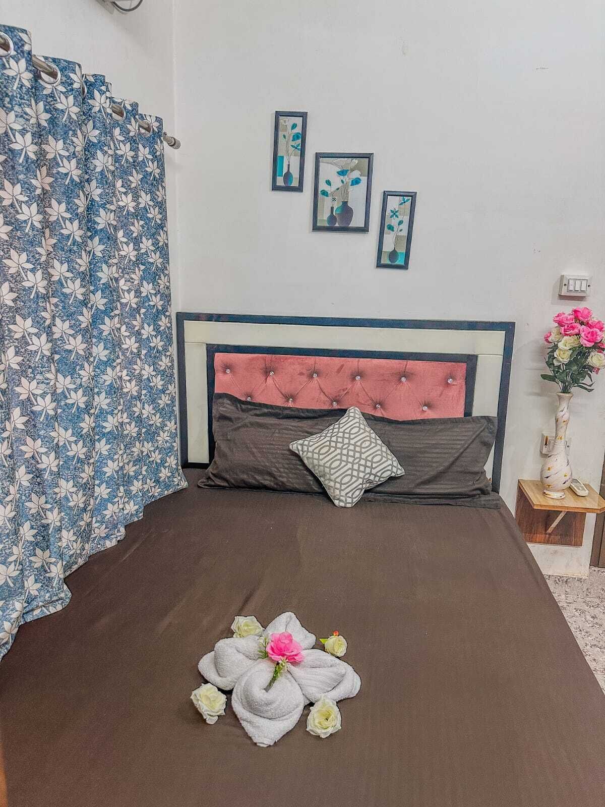 Een netjes opgemaakt bed met een bruine sprei, een gestuufd hoofdeinde en een decoratief kussen. Boven het bed hangen drie ingelijste foto’s aan de muur.