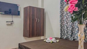 A bedroom with a bed, a wooden wardrobe, a wall-mounted TV, and a floral vase on a bedside table.