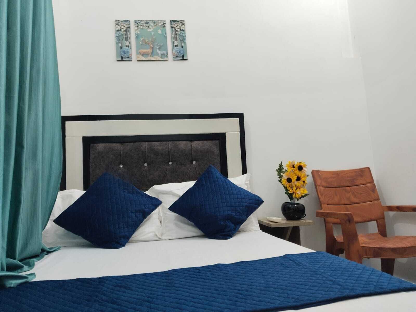A neatly made bed with blue bedding, a dark headboard, and a teal curtain. There are three wall-mounted pictures above the bed.