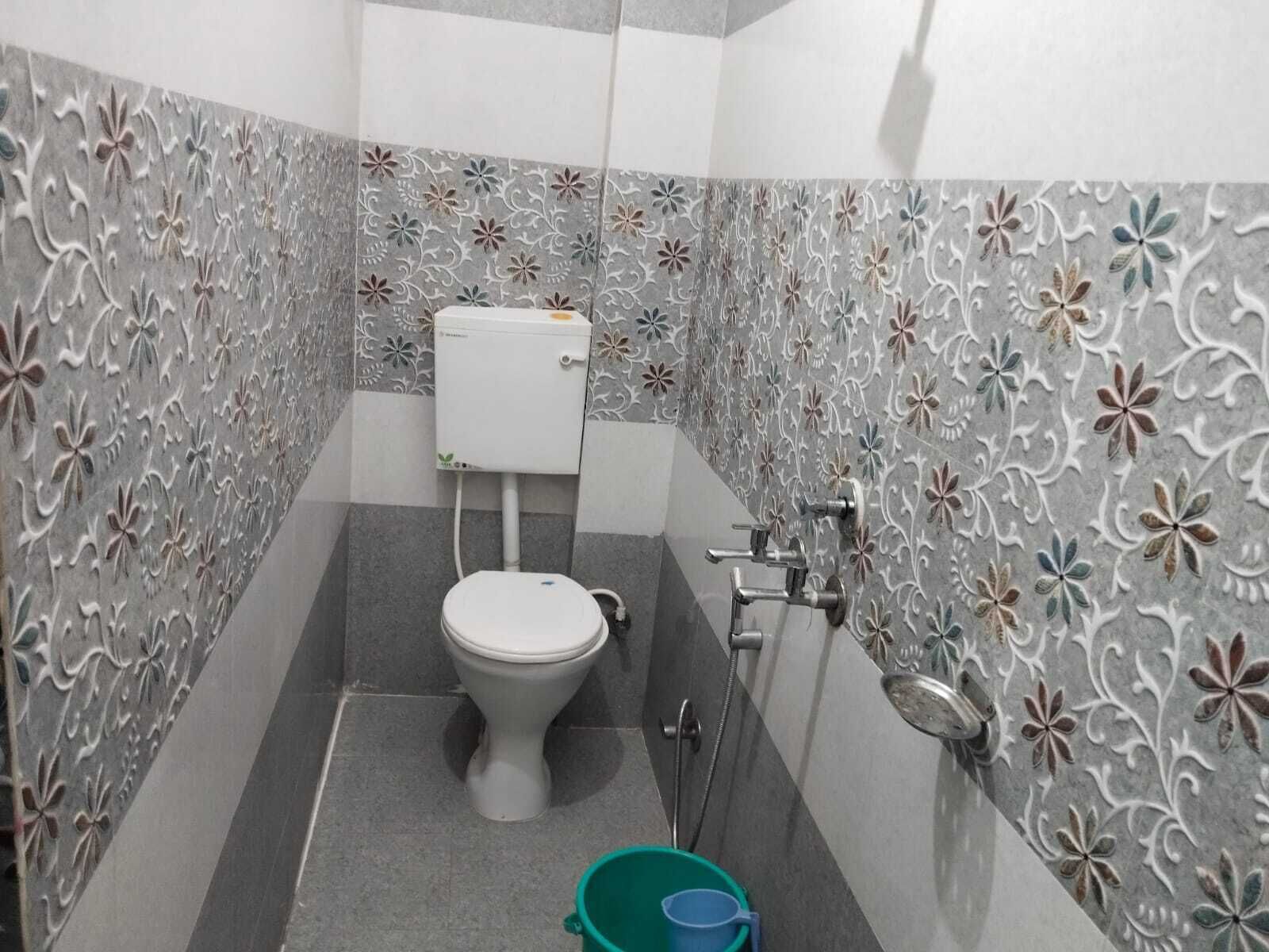 Een badkamer met toilet, douche en een groene emmer op de vloer.