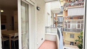 Un balcó amb zona de dinar, una porta corredissa de vidre i vista a edificis veïnals.