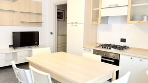 Cuina moderna amb taula de fusta, caires blancs, fogó i armaris integrats.