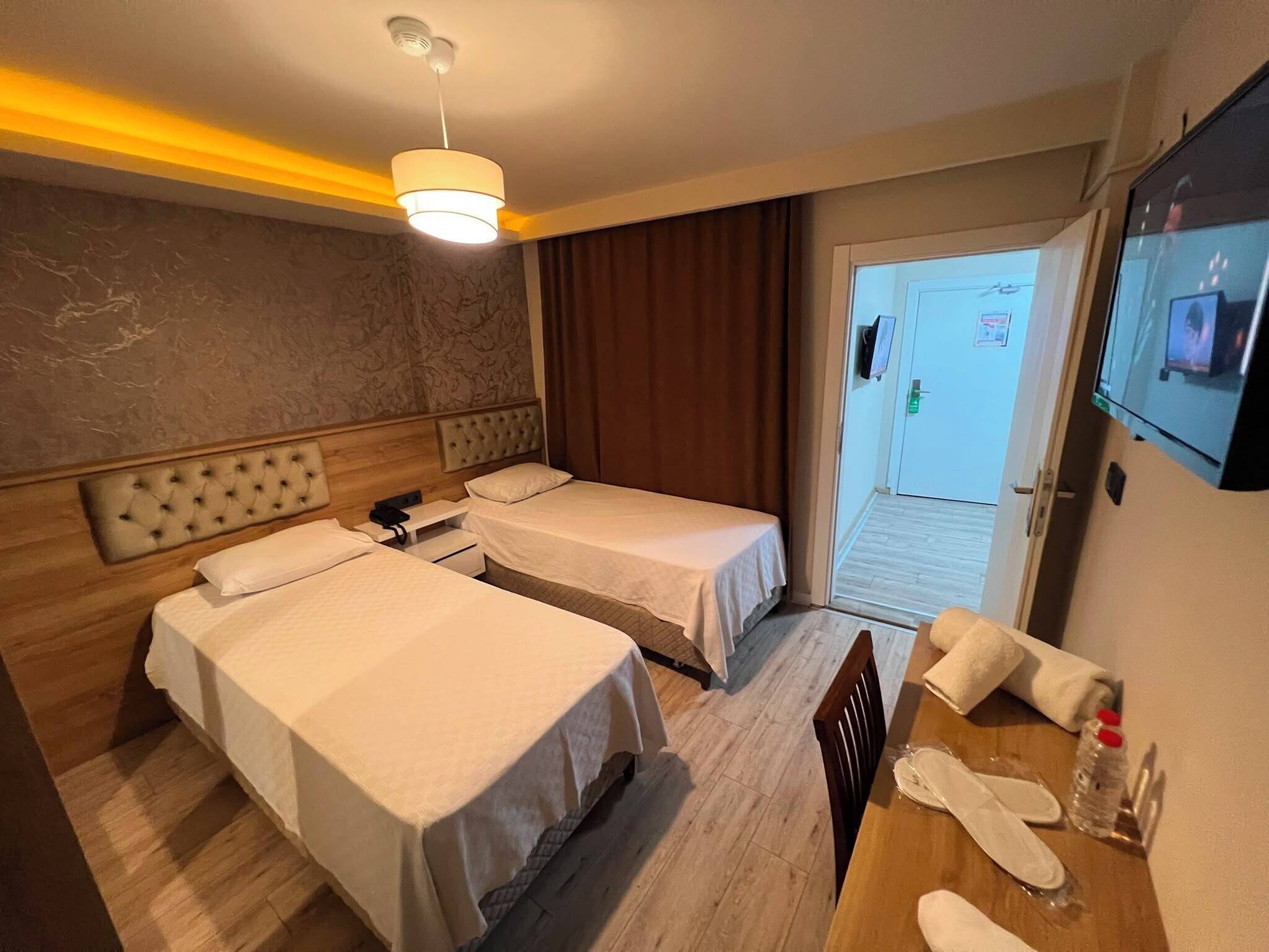 Ett hotellrum med två sängar, en sänggavel i trä, en tv och ett bord med en flaska och glas.
