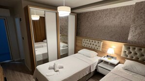 A hotel room with two beds, a bedside table with a lamp, a mirror, and a wardrobe.