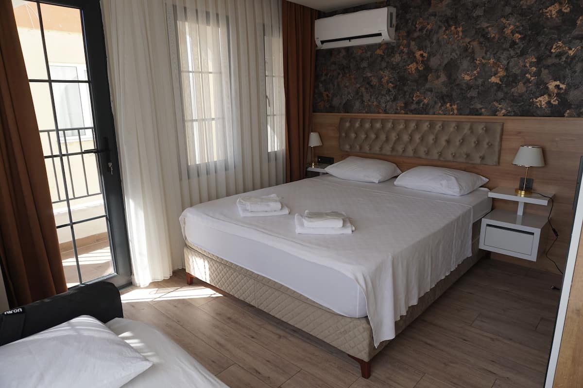 Una habitación de hotel con una cama grande, una mesita de noche con lámpara y un equipo de aire acondicionado en la pared.